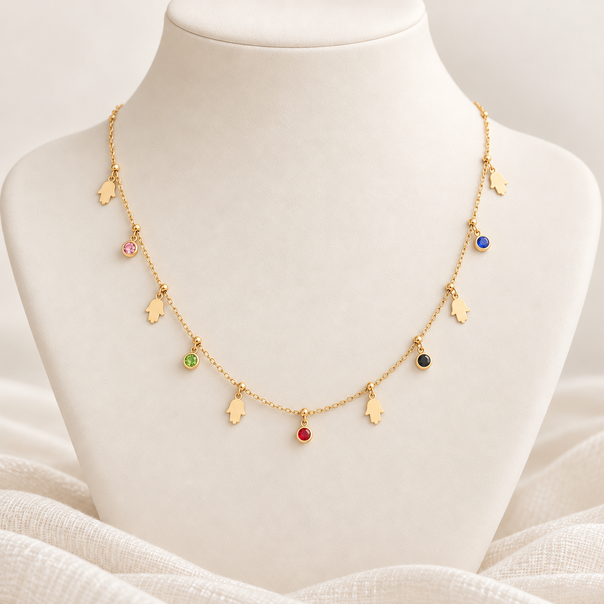 A delicate gold necklace displayed on a white jewelry bust. The necklace features small hand-shaped charms interspersed with tiny round gemstone pendants in pink, green, red, blue, black, and white.