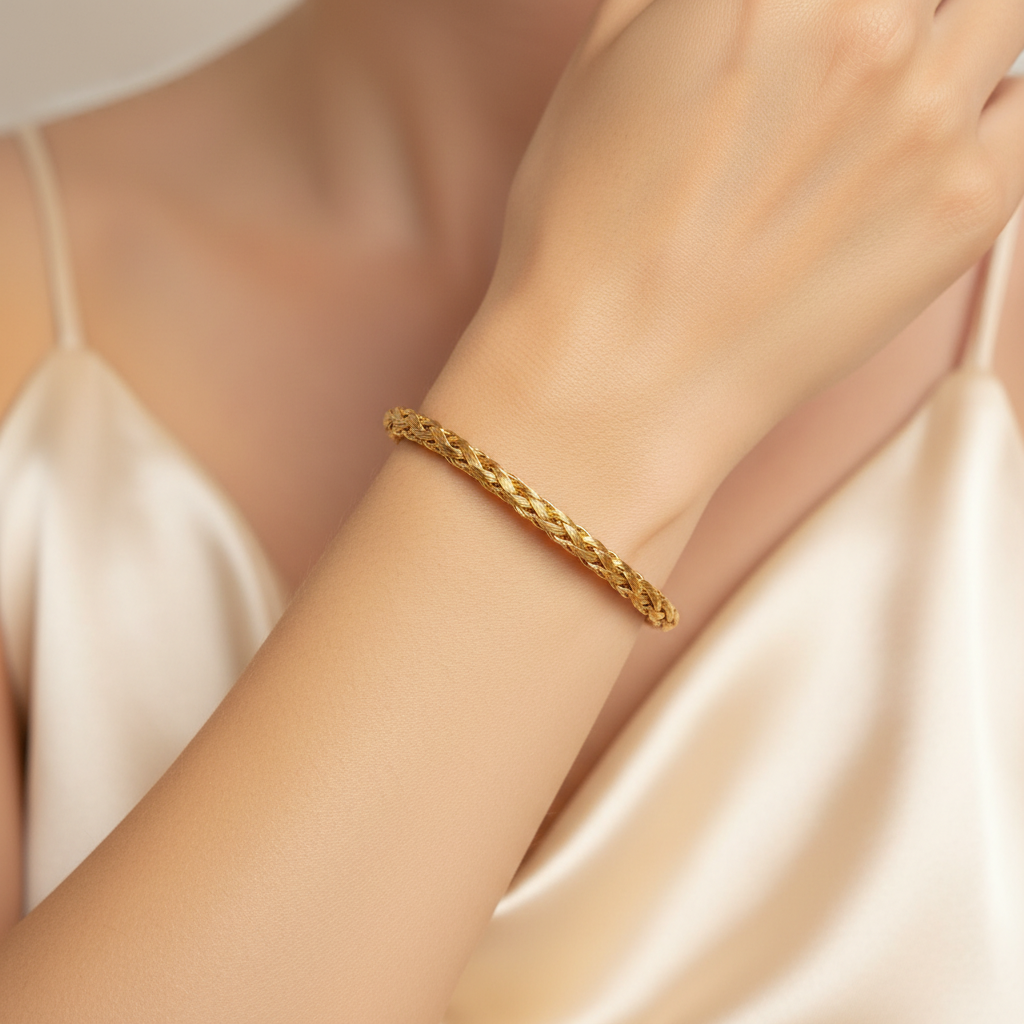 A gold-colored twisted rope cuff bracelet with an open end, displayed on a light wood grain surface.