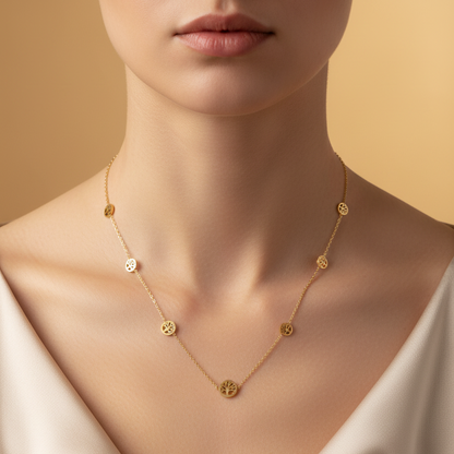A close-up of a model wearing a delicate gold necklace with small, evenly spaced circular gold charms, styled with a cream satin top against a warm beige background.