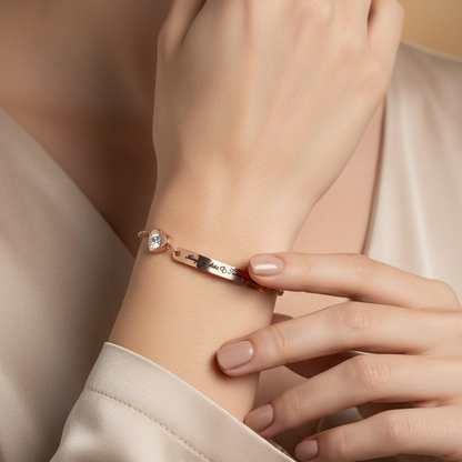 A close-up lifestyle shot of a model wearing a delicate rose gold bracelet with a small clear gemstone and a tiny red accent, styled with a beige satin top.