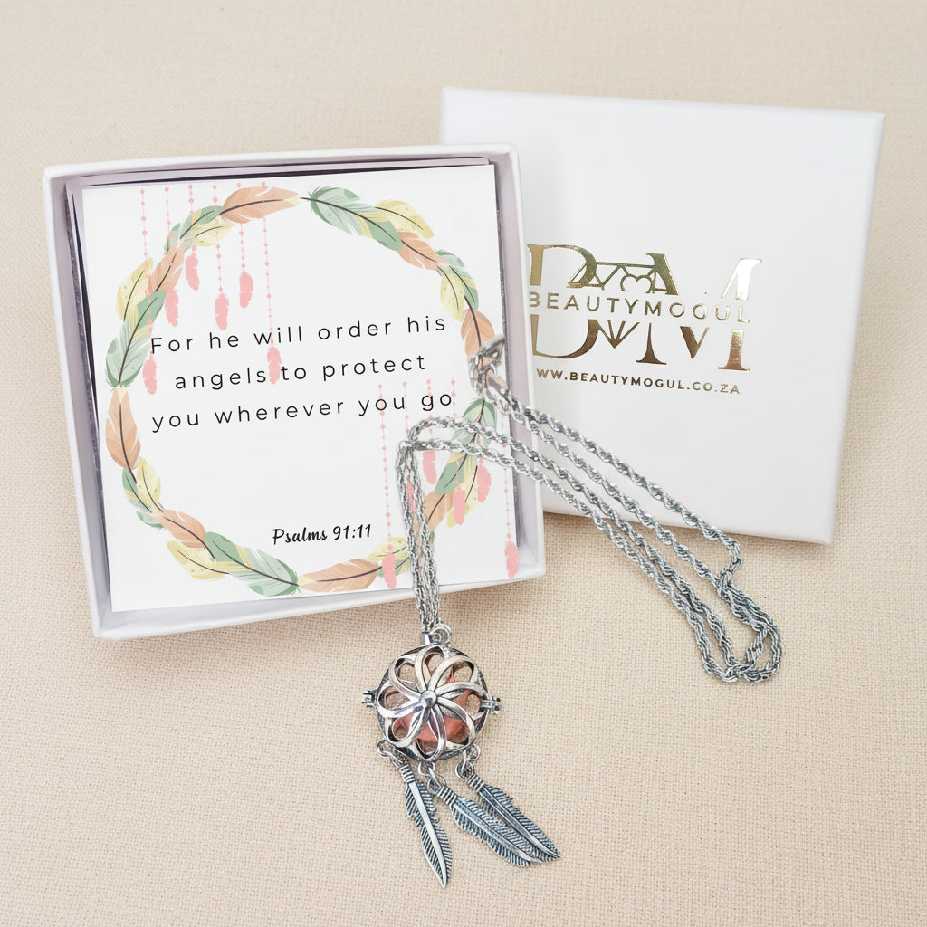 A silver-toned dreamcatcher pendant necklace with feather charms, displayed in front of its white gift box and card. The card features a watercolor wreath and the Bible verse Psalms 91:11.