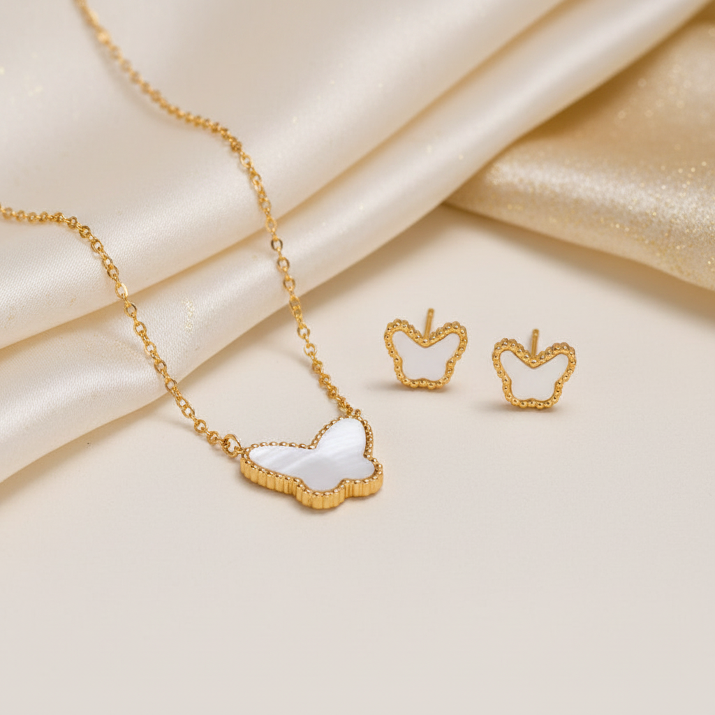 Gold jewelry set featuring a necklace and matching stud earrings with apple-shaped white inlay details, styled on a cream satin background.