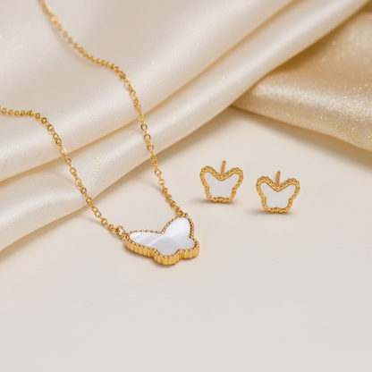 Gold jewelry set featuring a necklace and matching stud earrings with apple-shaped white inlay details, styled on a cream satin background.