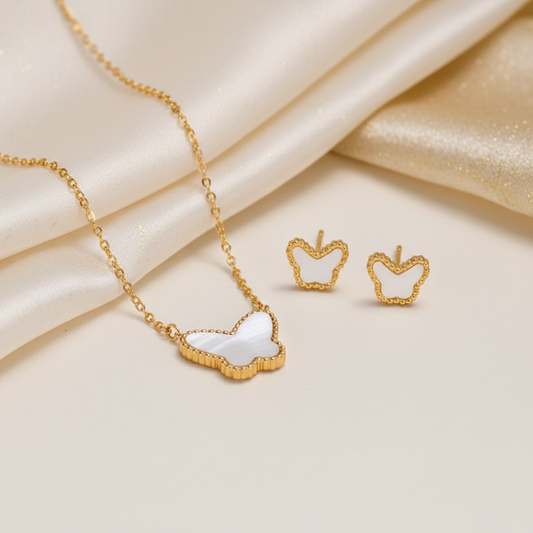Gold jewelry set featuring a necklace and matching stud earrings with apple-shaped white inlay details, styled on a cream satin background.