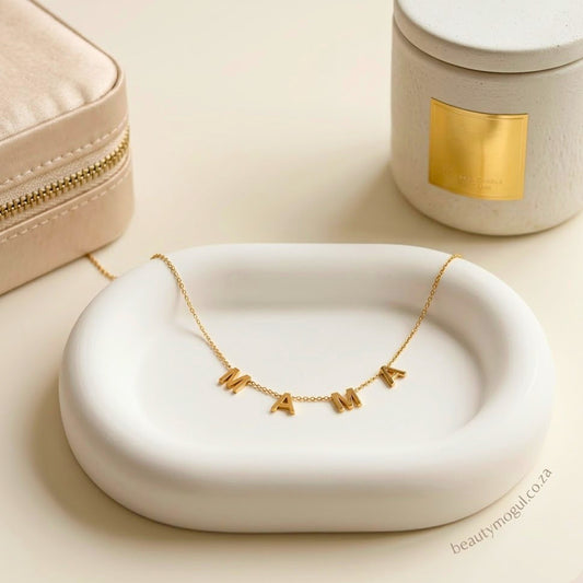 Gold MAMA script necklace elegantly draped on a white ceramic tray with Beautymogul branded jewellery box.