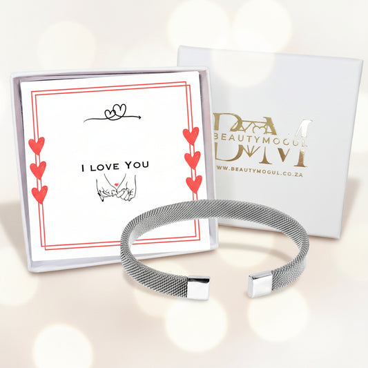 A silver mesh cuff bracelet displayed in front of its gift box and branded card. The box lid features the brand name 'BEAUTYMOGUL' in gold foil, and the inner card reads 'I LOVE YOU' with red hearts and a small heart detail.