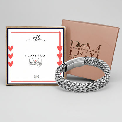 A silver braided chain bracelet displayed in front of a pink presentation box and a white gift card that reads 'I LOVE YOU' with small red hearts. The box is branded BEAUTYMOGUL.