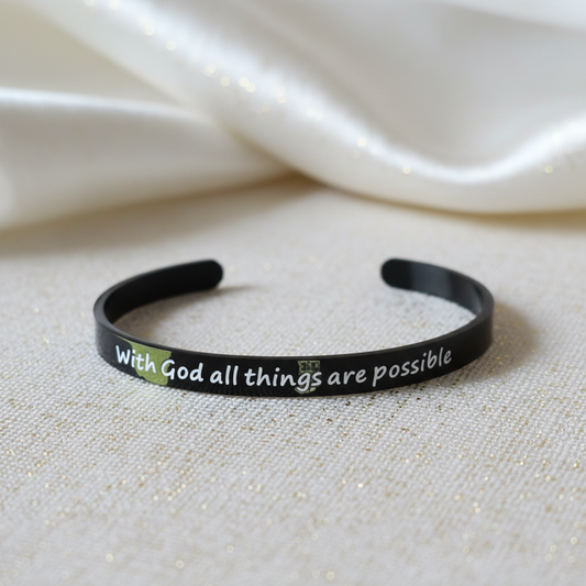 Beautymogul-A black metal cuff bracelet with the phrase 'With God all things are possible' printed in white, resting on a textured beige fabric with a soft white satin drape in the background.