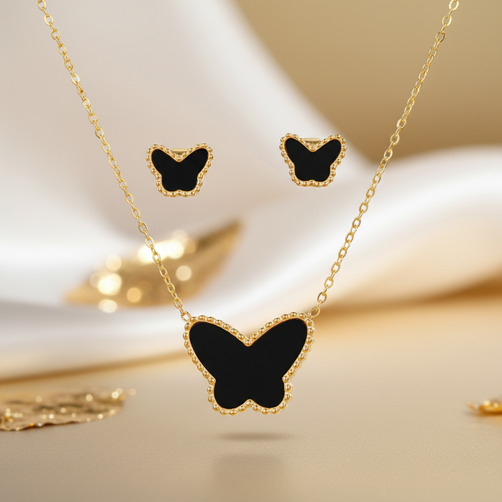 Gold-tone butterfly jewelry set featuring a pendant necklace and matching stud earrings with black inlay, displayed on a soft beige surface with a blurred background.