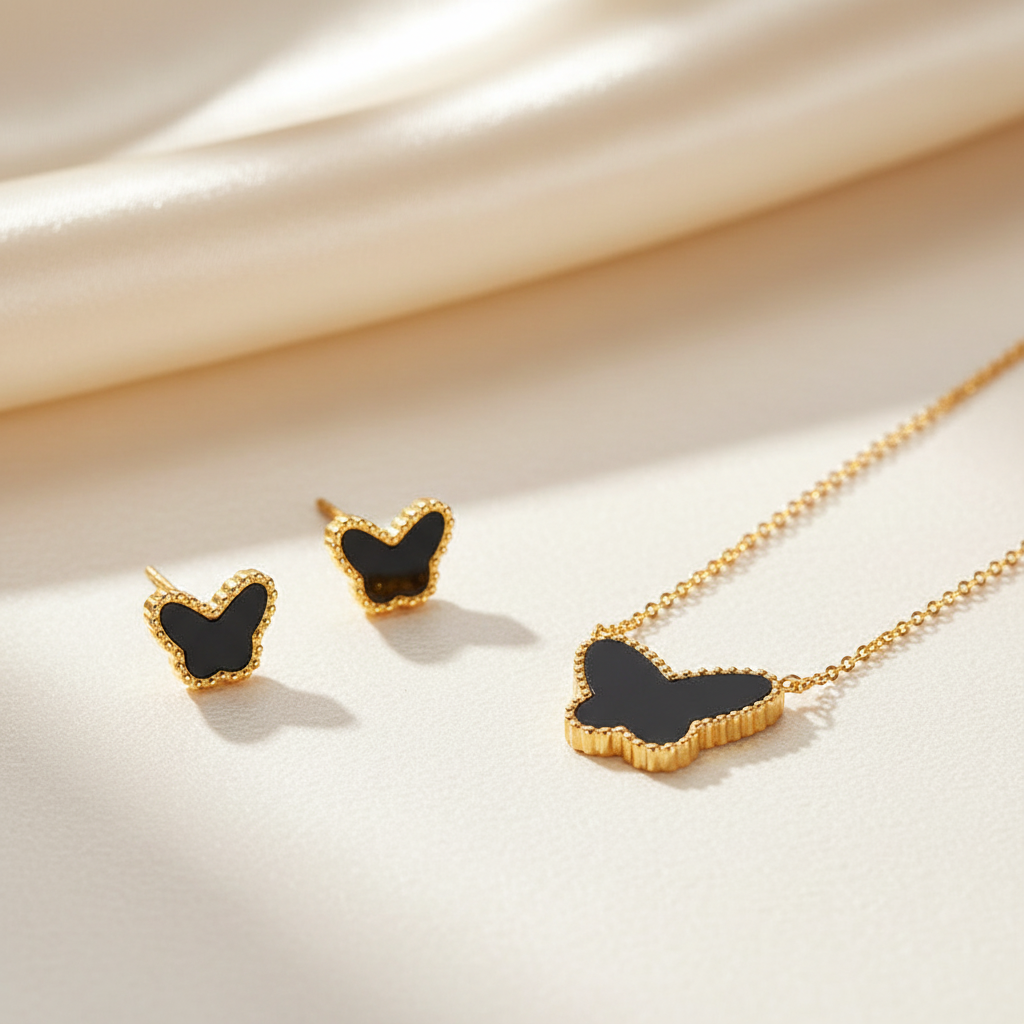 Gold butterfly jewelry set including a necklace and matching stud earrings with black inlay, arranged on a cream satin fabric background.