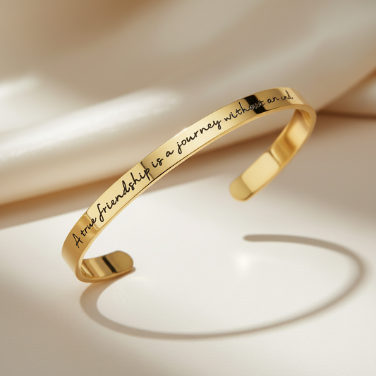 Beautymogul Gold Plated Friendship Journey bracelet- A polished gold cuff bracelet engraved with the quote 'True friendship is a journey without a map', displayed on a warm cream-colored surface with soft shadows.