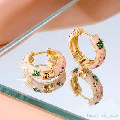 Gold hoop earrings with pink and green accents on a reflective surface