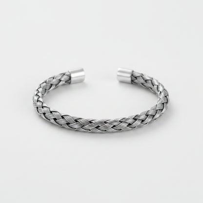 A silver braided cuff bracelet with a textured woven pattern and polished metal end caps, displayed on a clean light gray background.