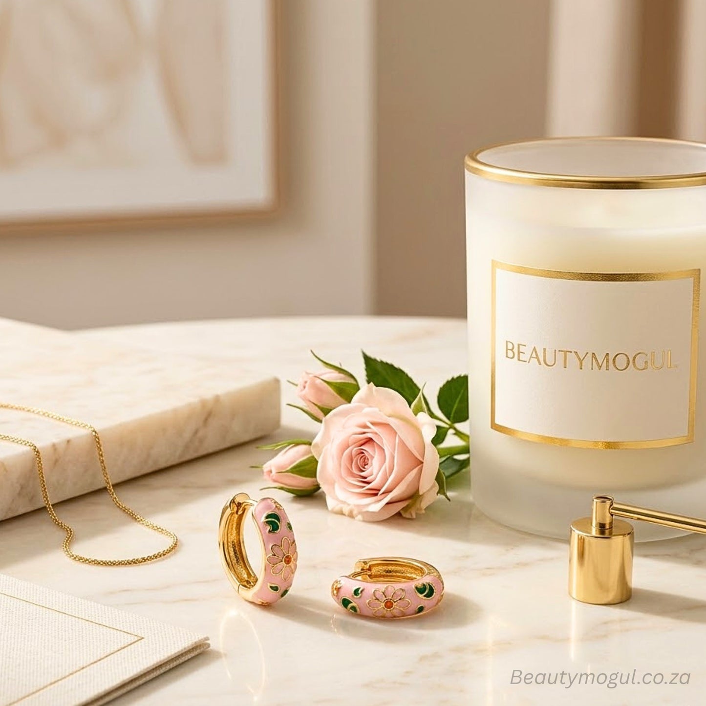 Jewelry set with pink floral design next to a candle labeled 'BEAUTYMOGUL' on a marble surface.