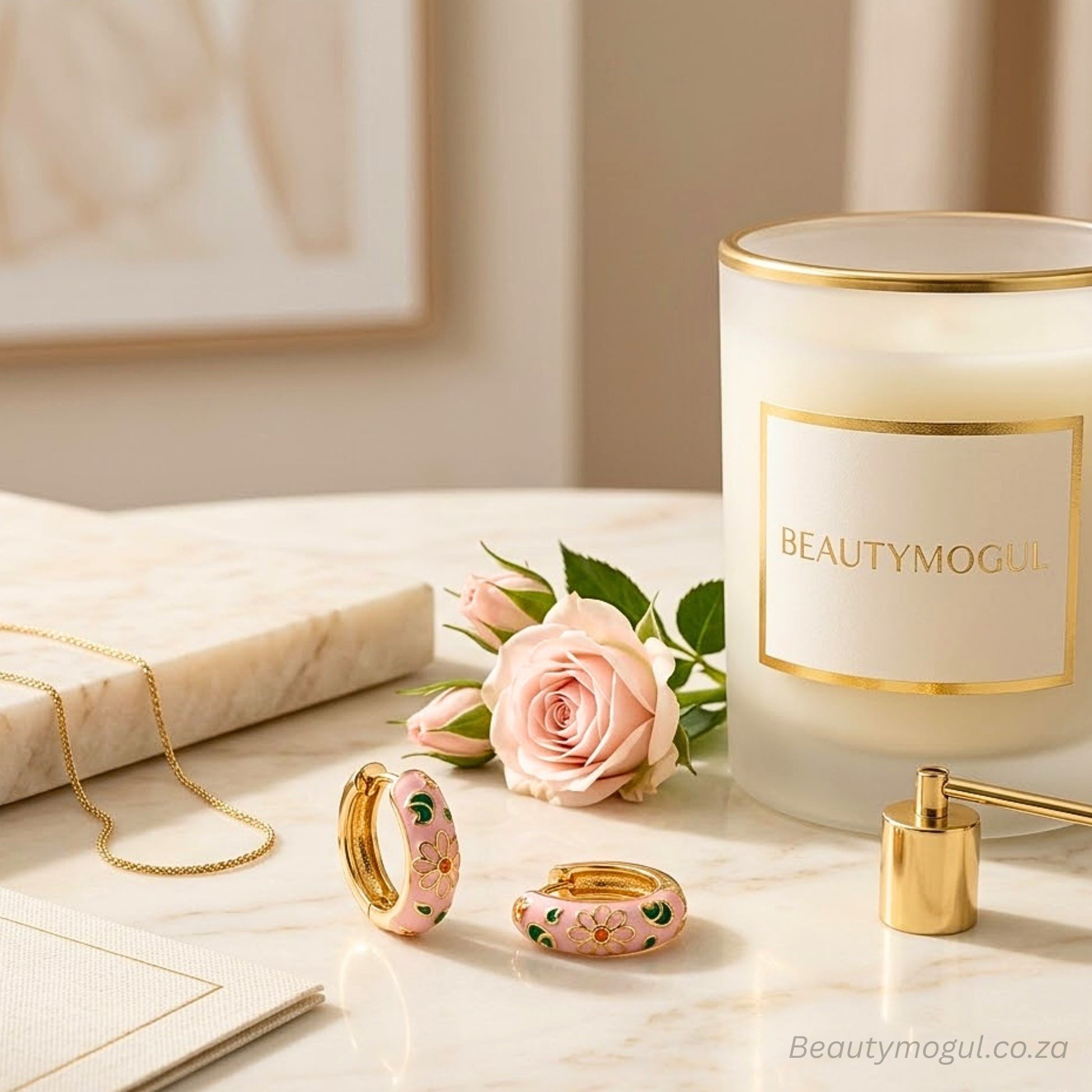 Jewelry set with pink floral design next to a candle labeled 'BEAUTYMOGUL' on a marble surface.