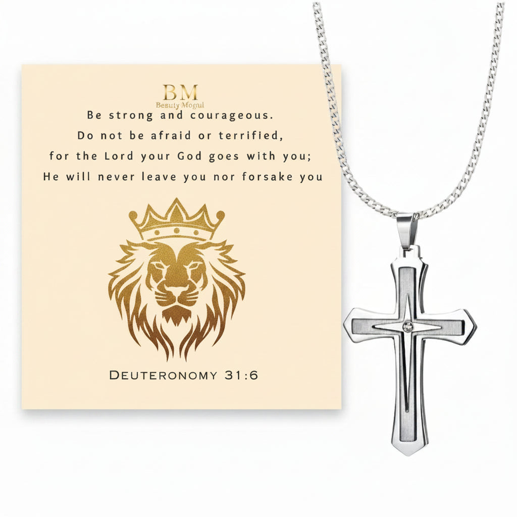 Silver cross pendant necklace displayed next to a cream-colored card featuring a gold lion illustration, the text 'Be strong and courageous' from Deuteronomy 31:6, and a small 'BM' monogram.