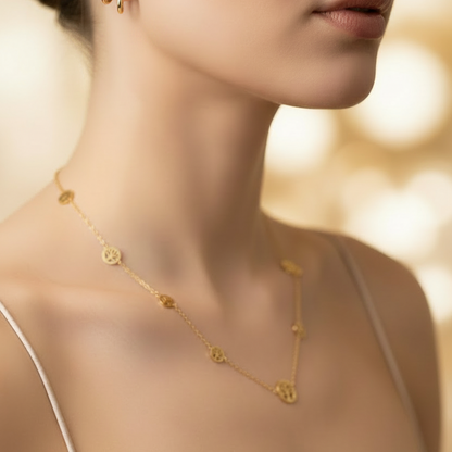 A close-up lifestyle shot of a model wearing a delicate gold necklace with small circular medallions and matching gold hoop earrings, styled with a satin cream top against a warm, softly blurred background.