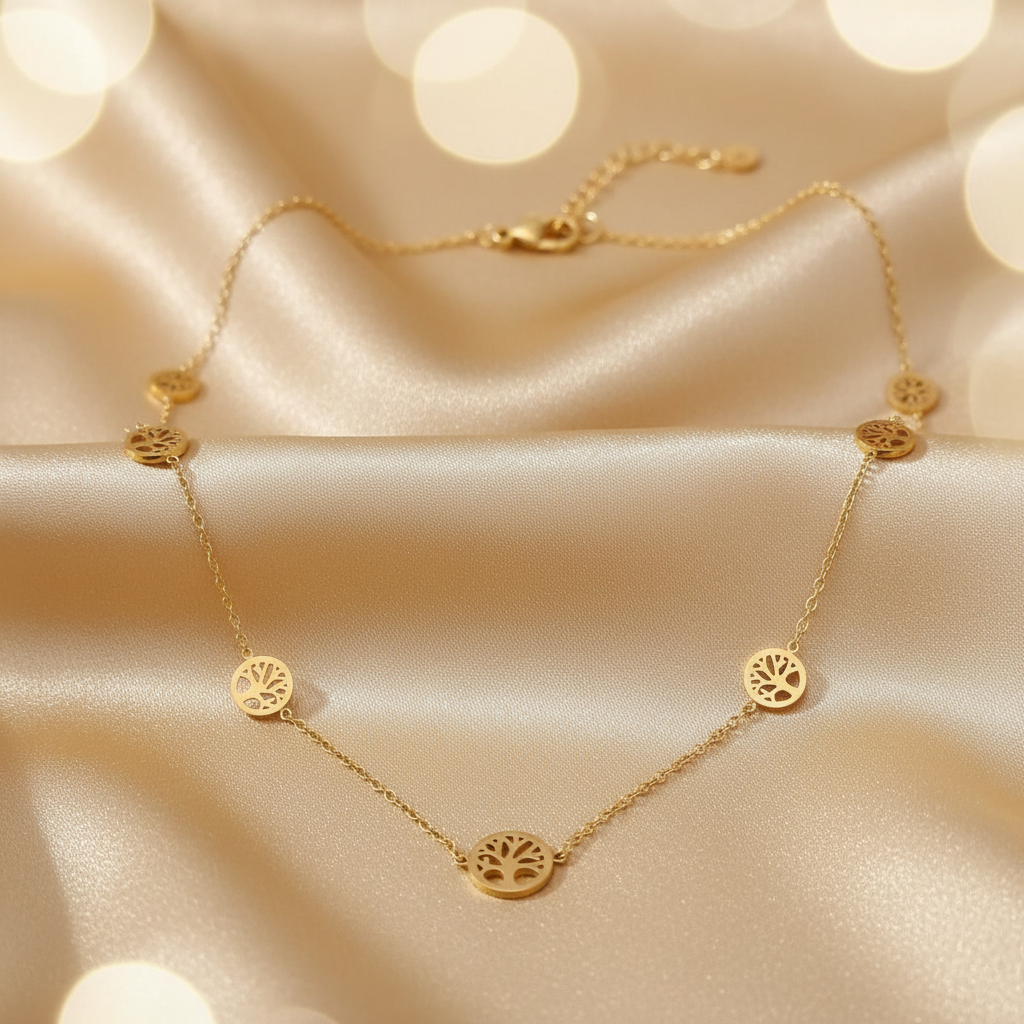 A delicate gold necklace with five circular tree-of-life pendant charms, displayed on draped champagne satin fabric with soft bokeh light effects in the background.