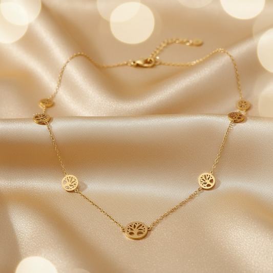 A delicate gold necklace with five circular tree-of-life pendant charms, displayed on draped champagne satin fabric with soft bokeh light effects in the background.