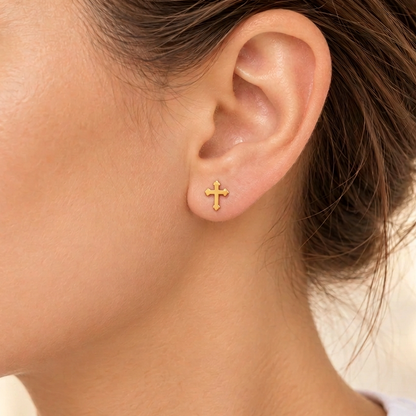 A close-up of a woman's ear wearing a small gold cross stud earring.