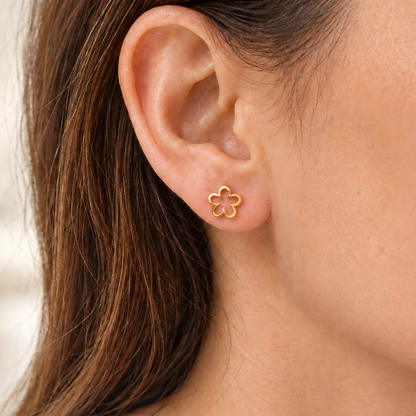 A close-up of a woman's ear wearing a small gold flower-shaped stud earring.