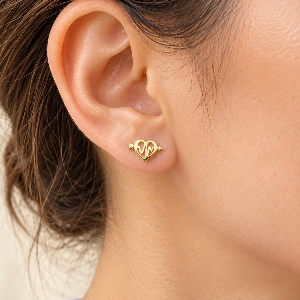 Close-up of a woman in a white T-shirt wearing a dainty gold-tone heartbeat heart stud.