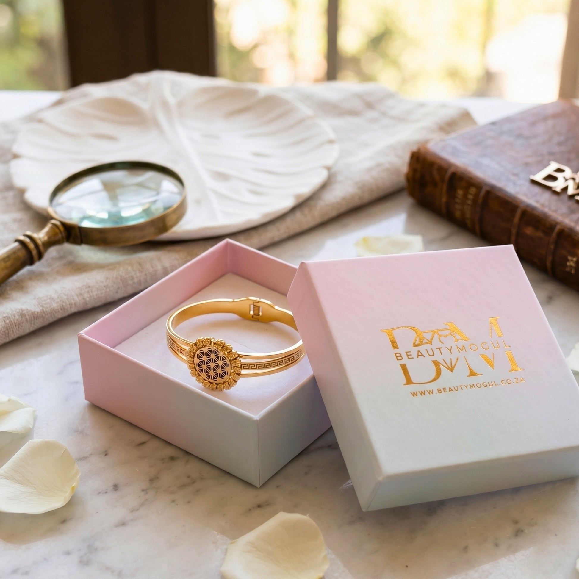 Gold plated bracelet beautymogul branding on a marble surface.