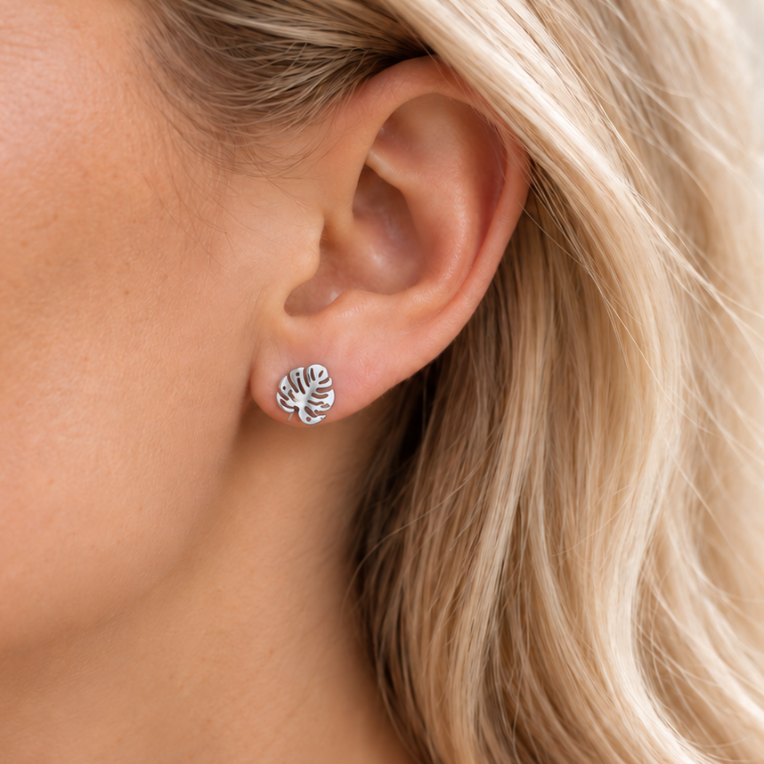 Close-up of a model wearing a dainty silver monstera leaf stud earring with a white linen top.