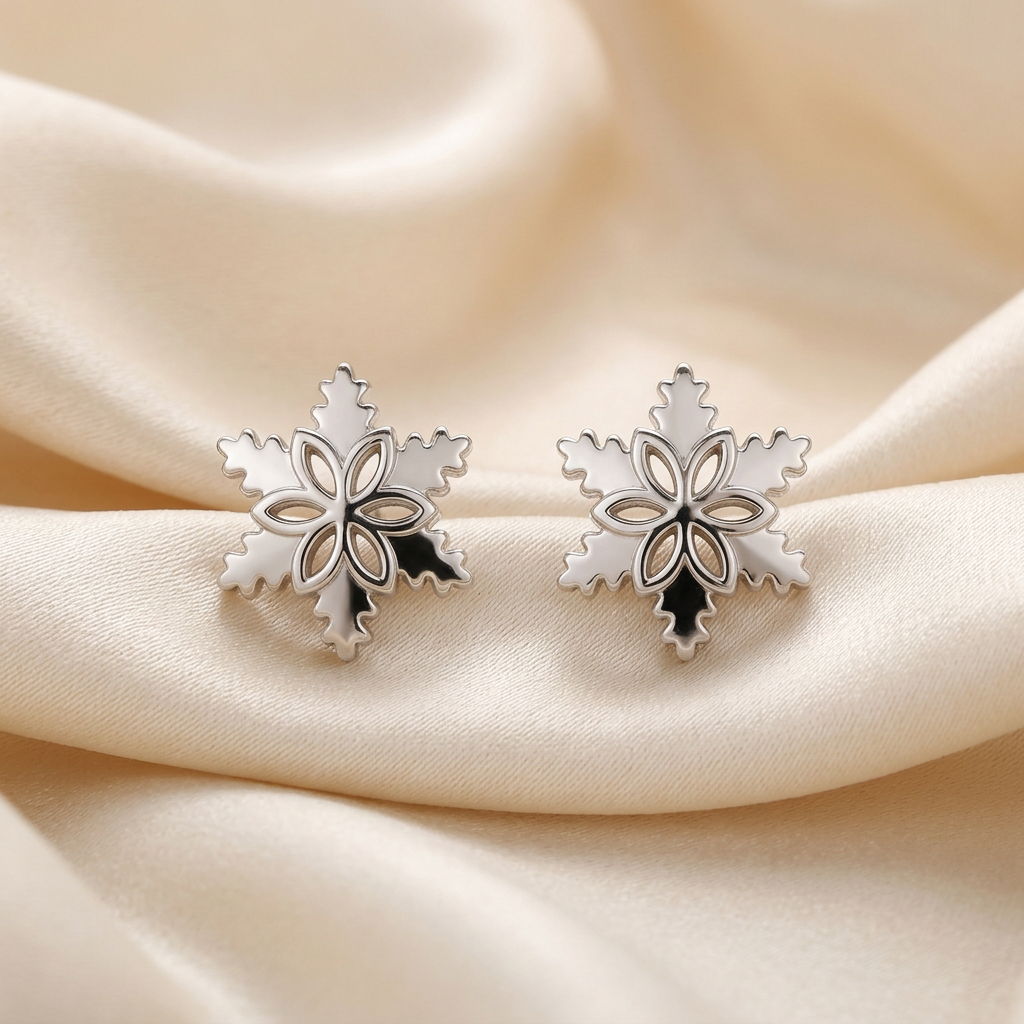 Pair of silver-tone snowflake stud earrings with floral centres displayed on champagne satin.