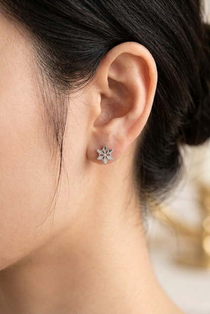 Close-up of a woman wearing a silver-tone snowflake stud earring with a delicate floral centre.