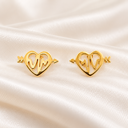 A pair of gold heart-shaped stud earrings with an openwork design, displayed on a draped cream satin fabric background.